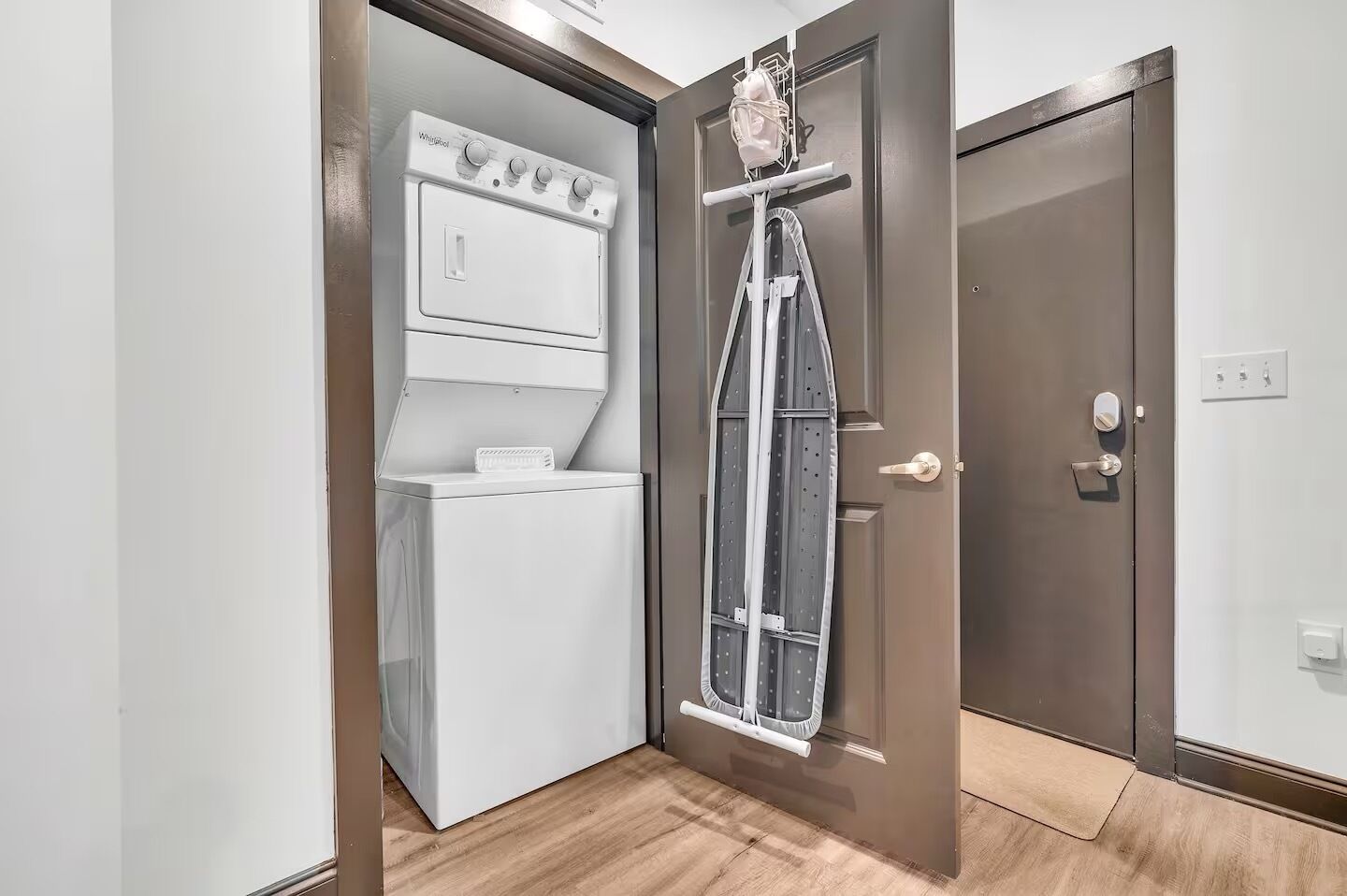 A compact laundry room with a washer and dryer, a drying rack, and a door with a handle.