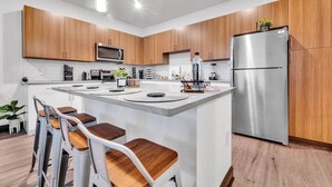 Une cuisine moderne avec des meubles en bois, un réfrigérateur en acier inoxydable, un four à micro-ondes et un îlot central doté de tabourets de bar.