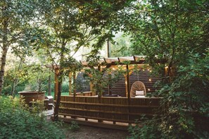 Una terraza de madera con zona de estar, rodeada de árboles.