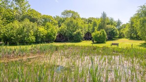 A rustic cabin with a wooden deck, surrounded by lush greenery and a pond.