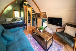 Une chambre à coucher confortable, aménagée en style « loft », avec un lit, un canapé bleu, une table basse en bois et un téléviseur.