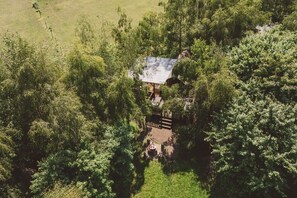 Une vue aérienne d’un chalet isolé, entouré d’une forêt dense, avec une terrasse bien visible et un petit espace de détente extérieur.