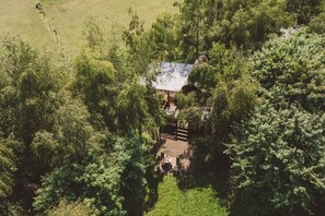 Une vue aĂ©rienne dâun chalet isolĂ©, entourĂ© dâune forĂȘt dense, avec une terrasse bien visible et un petit espace de dĂ©tente extĂ©rieur.