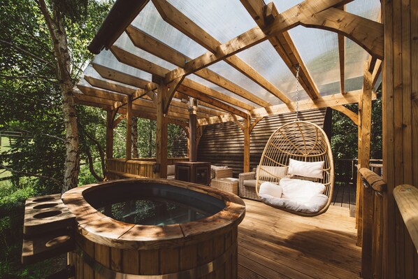 Une terrasse en bois avec un jacuzzi, des fauteuils en osier et un plafond en verre.