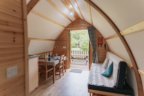Ein gemütliches, holzgetäfeltes Interieur mit Essbereich, einer Couch mit Kissen und Blick auf die Terrasse.