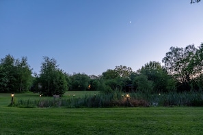 Un parque al anochecer con árboles, un banco y un edificio distante.