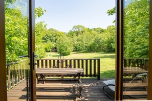 Eine Holzterrasse mit Bank und Tisch, mit Blick auf eine Wiese mit Bäumen.
