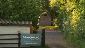 A sign for Wigwam Holidays at Charwood Forest, with a rustic wooden fence and a path leading to a barn.