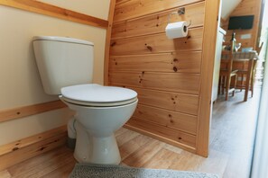 Un baño con paneles de madera, un inodoro blanco, un mueble de madera y un dispensador de papel higiénico a la vista.