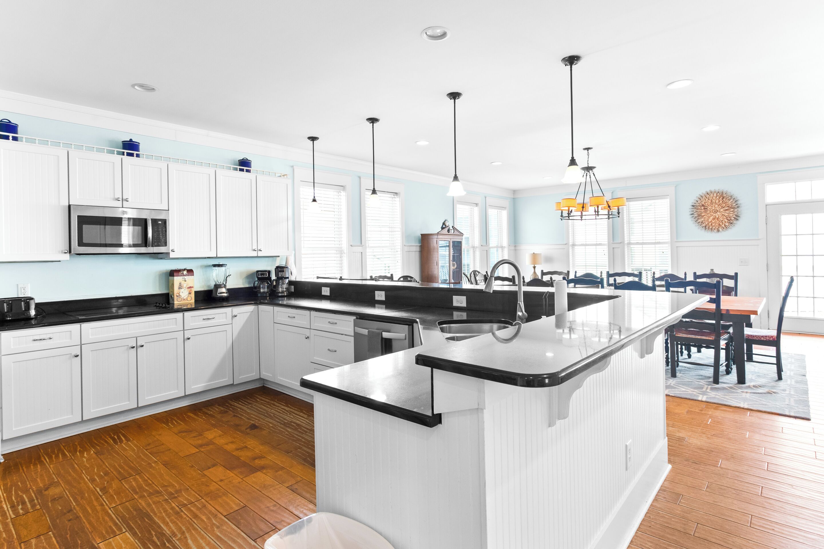 Una cocina moderna con armarios blancos, una isla central y una zona de comedor con candelabro.