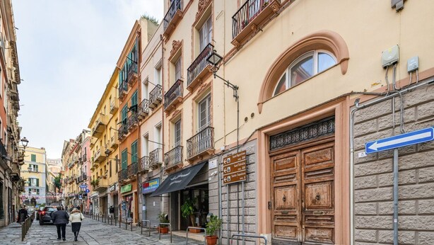A cobblestone street lined with multi-story buildings, some with balconies and storefronts. - Alice House - Cagliari (Cagliari)