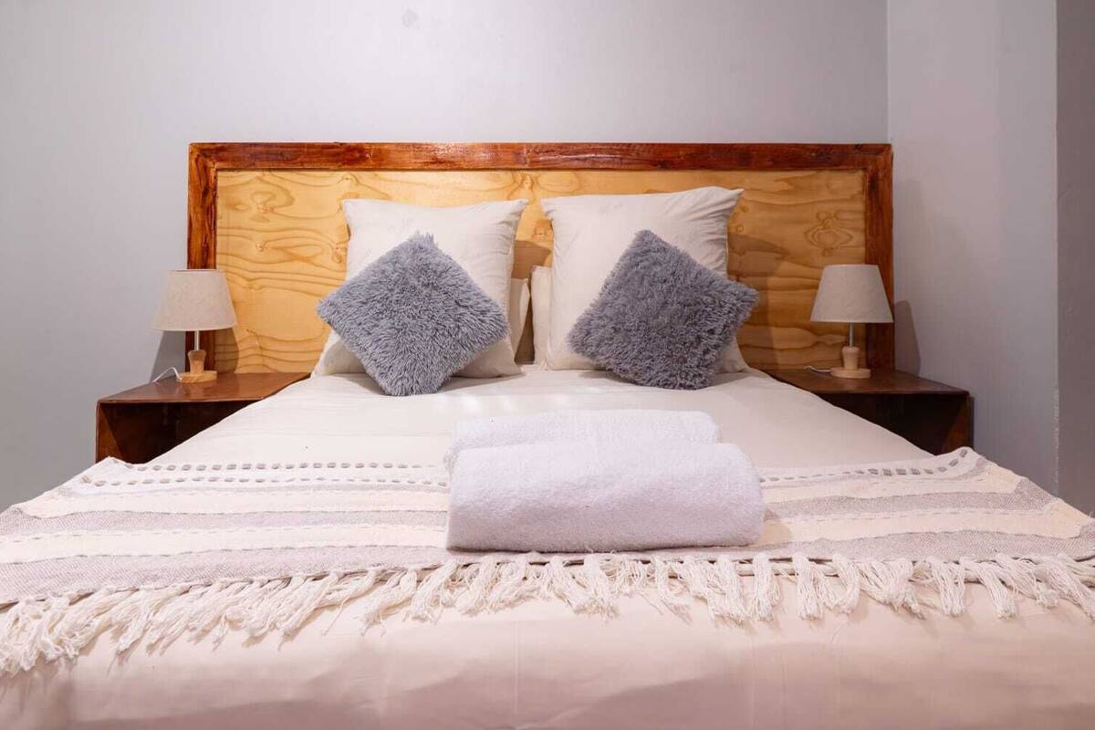 Ein ordentlich bezogenes Bett mit Holz-Kopfteil, zwei Kissen, einem gefalteten Handtuch und zwei Nachttischlampen.