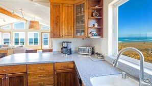 Una cocina con armarios de madera, cafetera, tostadora y vista al océano.