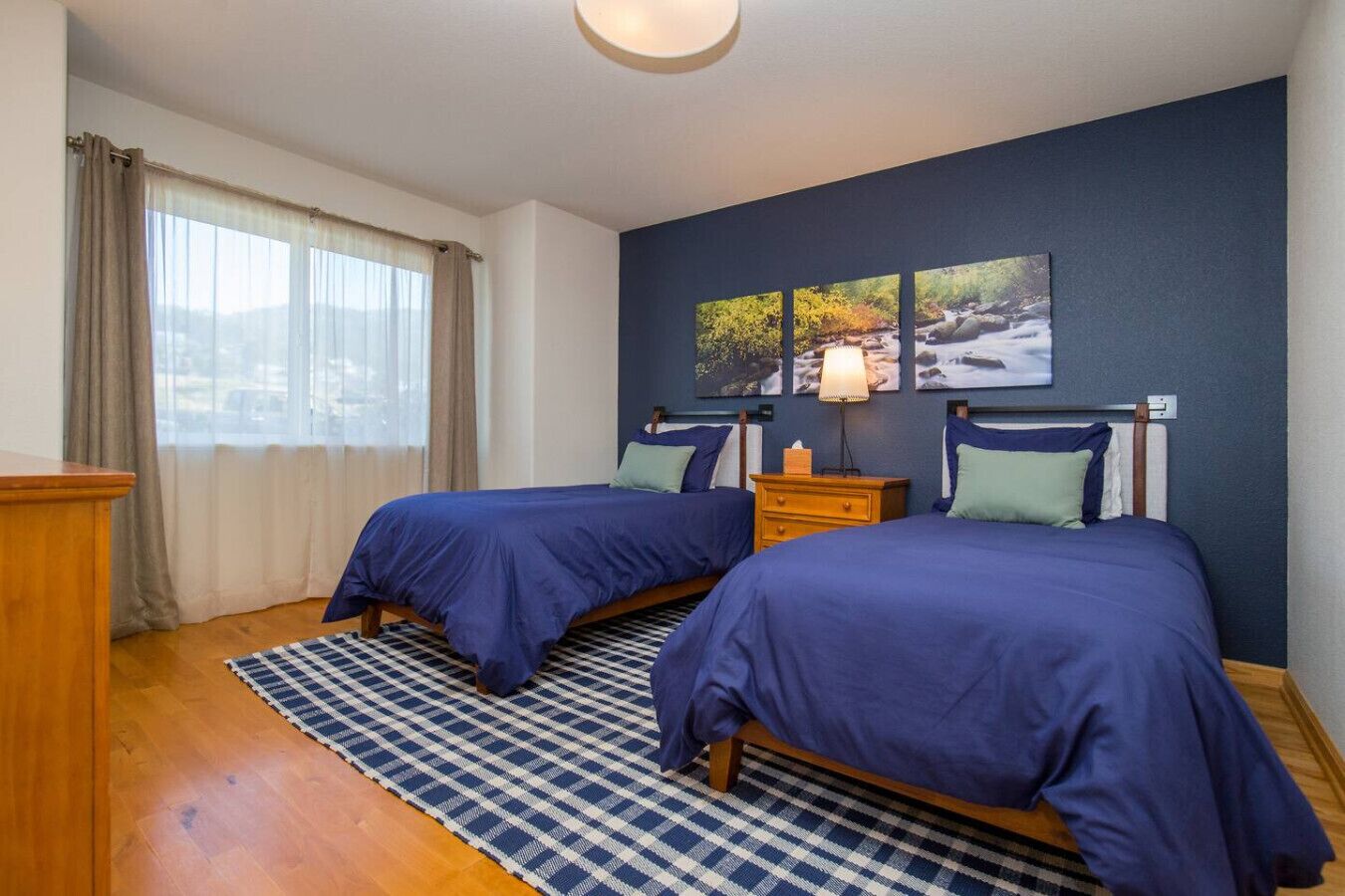 Ein Schlafzimmer mit zwei Betten, einem karierten Teppich, einem Nachttisch und einem Fenster mit Vorhängen.