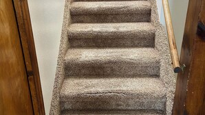 Un escalier recouvert de moquette, avec des rampes en bois et un cadre de porte en bois.