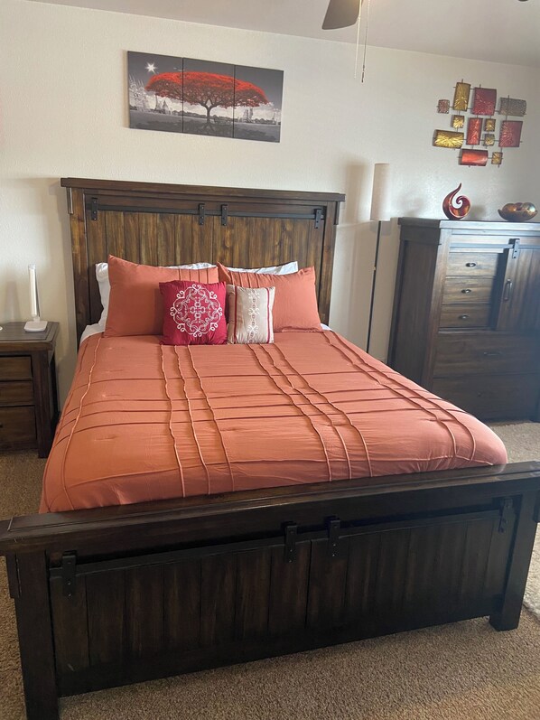 Een slaapkamer met een houten bed, nachtkastje, lamp, decoratief wandobject en een kast.