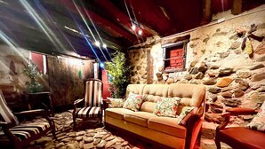 Una habitación acogedora con suelo de piedra, un sofá con cojines, sillas a rayas y una mesa de madera.