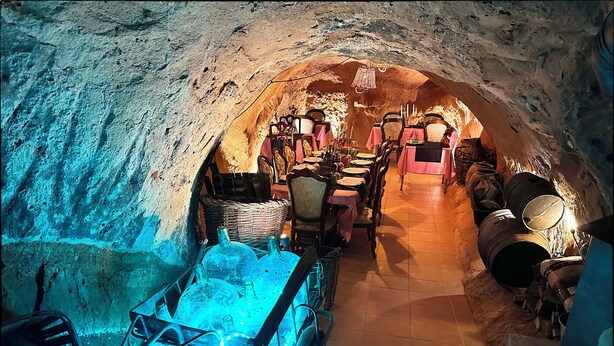 Un comedor subterráneo con decoración rústica, que incluye paredes de piedra, mesas y sillas de madera.