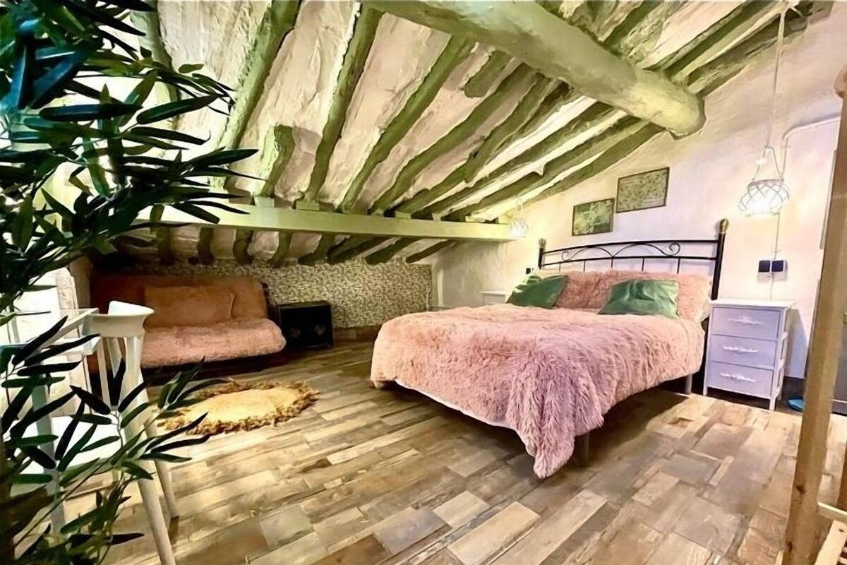 A cozy bedroom with a sloped ceiling, a bed with a fluffy pink blanket, a small sofa, and a nightstand.
