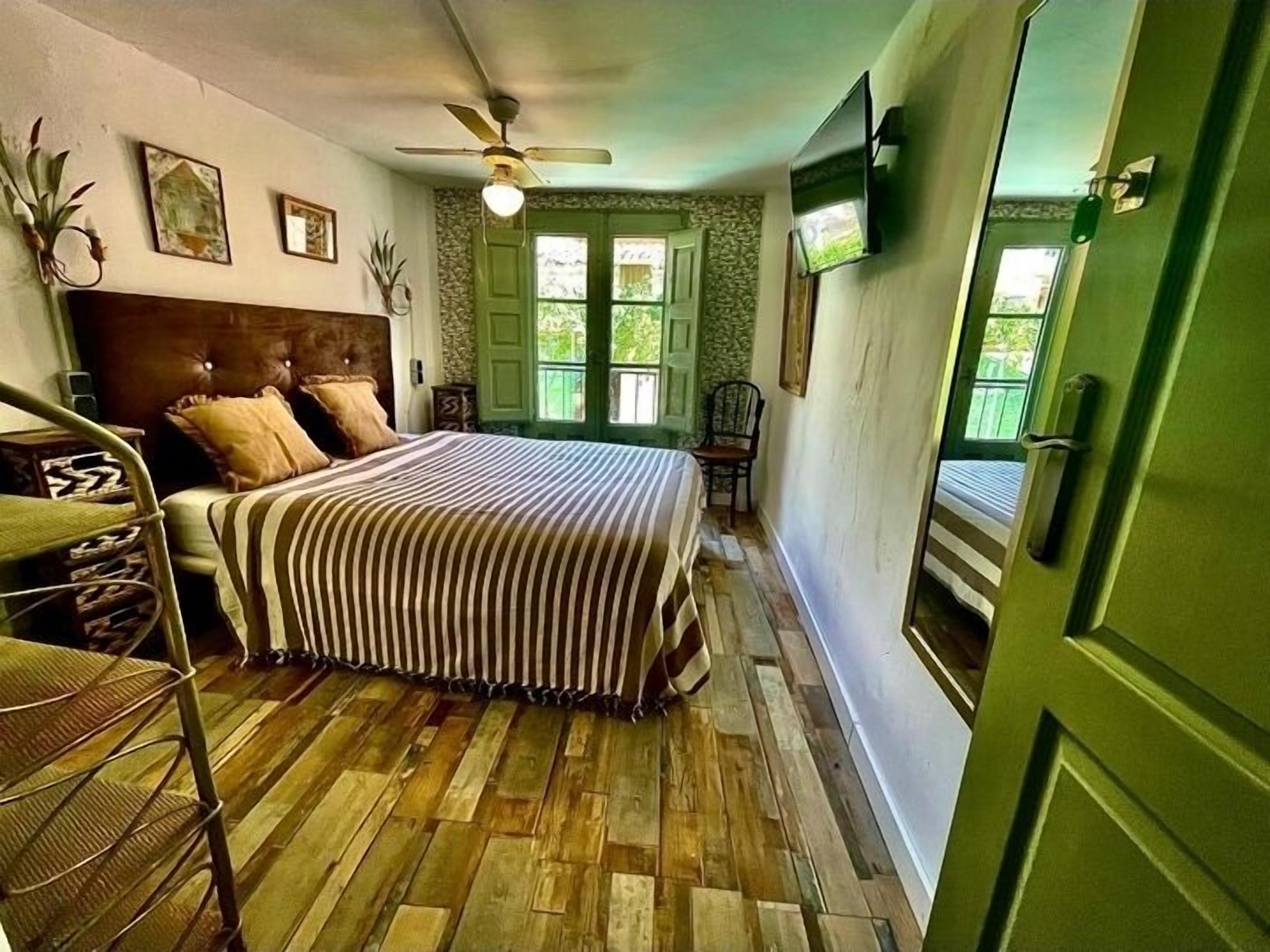 A bedroom with a bed, a chair, a ceiling fan, and a green door.