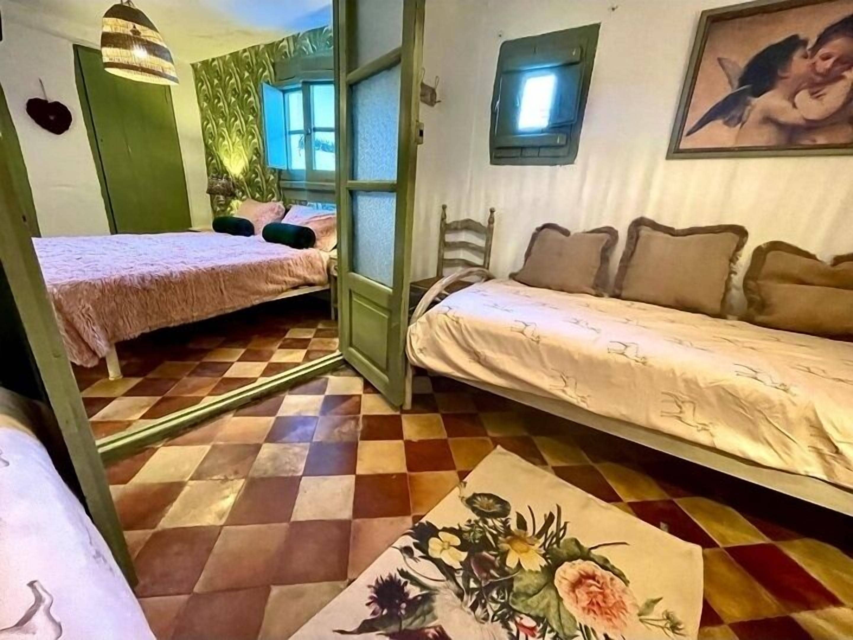 Een kamer met twee bedden, een groene deur, een raam en een schilderij aan de muur.