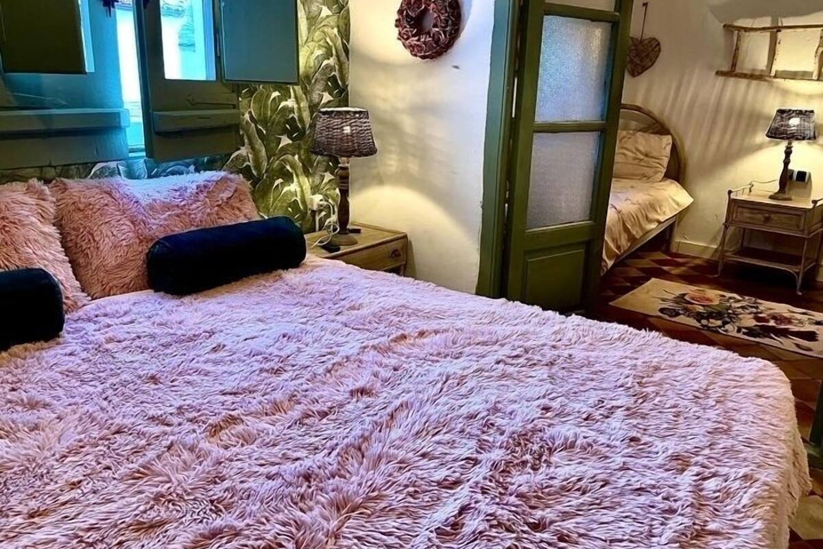 A bedroom with a large bed, a nightstand, a lamp, and a door leading to another room.