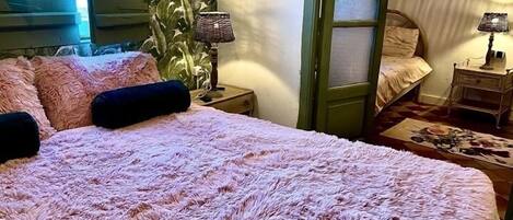 A bedroom with a large bed, a nightstand, a lamp, and a door leading to another room.