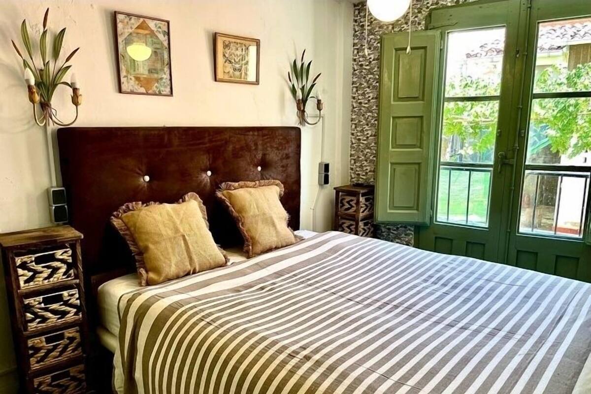 A bedroom with a striped bedspread, two pillows, a wooden headboard, and a green door with windows.