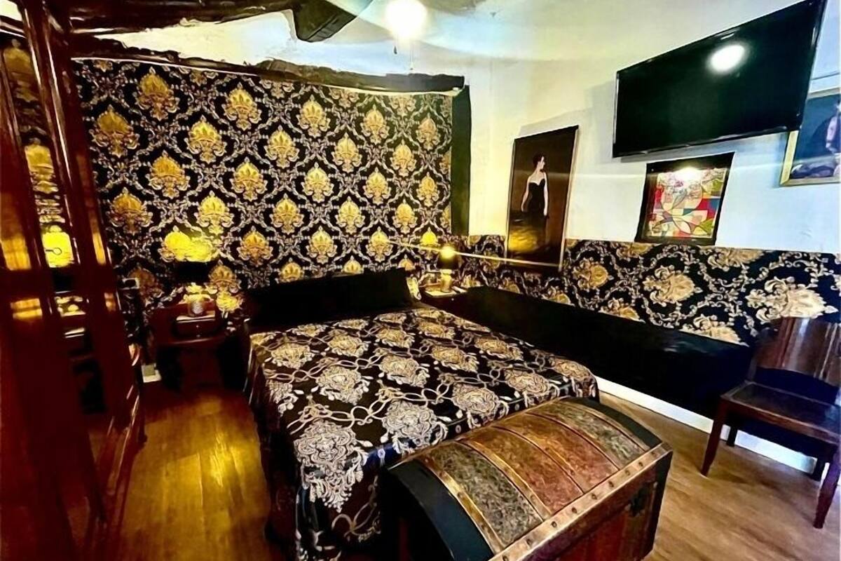 A room with a large bed, a bench, a TV, and a patterned wall.