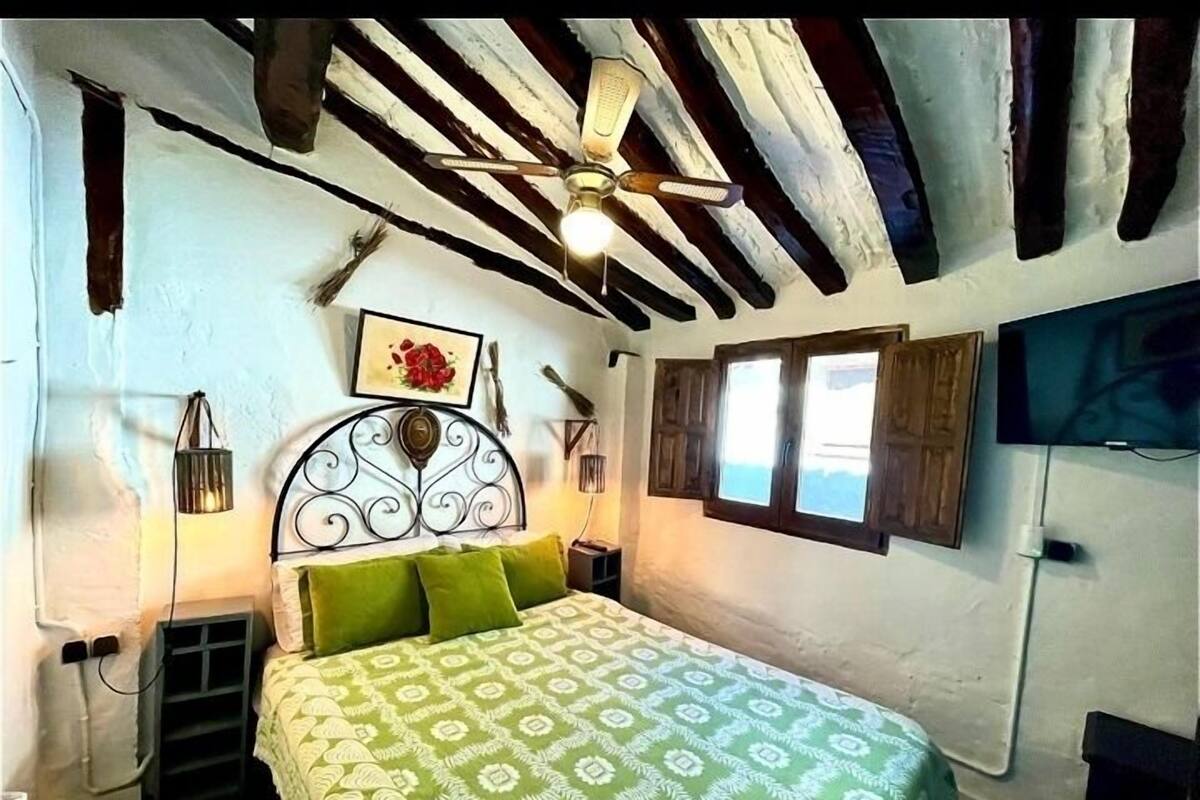 A bedroom with a bed, a ceiling fan, a window, and a TV.