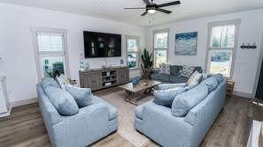 A living room with a grey sofa set, a coffee table, a TV, and a ceiling fan. - FREE Heated Pool! Sleeps 14 with Game Room! Close to Pier Park, Beaches & 30A! (Panama City Beach)