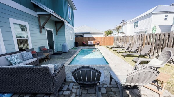 Un patio trasero con piscina, mobiliario exterior y una valla de madera.