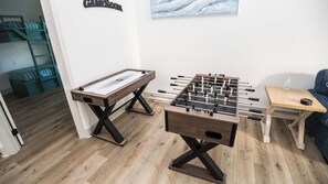Una habitación con dos mesas de fútbol de mesa, otra mesa de fútbol de mesa, una mesita con una botella y un sofá azul.