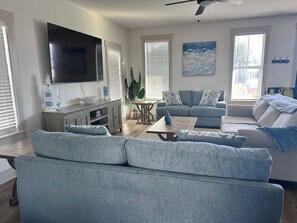 A modern living room with a flat-screen TV, a dining table, and a sofa set. - FREE Heated Pool! Sleeps 14 with Game Room! Close to Pier Park, Beaches & 30A! (Panama City Beach)