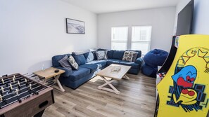 A living room with a blue sofa, a foosball table, and a coffee table. - FREE Heated Pool! Sleeps 14 with Game Room! Close to Pier Park, Beaches & 30A! (Panama City Beach)
