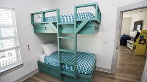 Una cama litera con escalera integrada, una ventana con persianas y una puerta que da a otra habitación.