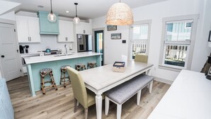 A modern kitchen with white cabinets, a teal accent wall, a central island with bar stools, and a dining table with a bench.