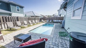 Un patio trasero con piscina, sillas de descanso, una mesa y una manguera.