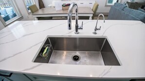 A kitchen with a white marble countertop, stainless steel sink, and two faucets.