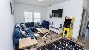 A living room with a sofa, coffee table, foosball table, and a Pac-Man arcade machine. - FREE Heated Pool! Sleeps 14 with Game Room! Close to Pier Park, Beaches & 30A! (Panama City Beach)