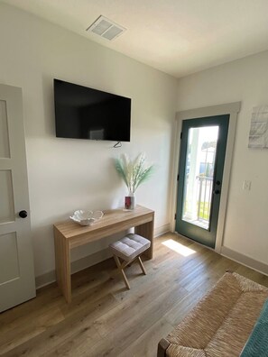 A room with a wooden desk, a television mounted on the wall, a door with a glass panel, and a woven rug on the floor. - FREE Heated Pool! Sleeps 14 with Game Room! Close to Pier Park, Beaches & 30A! (Panama City Beach)