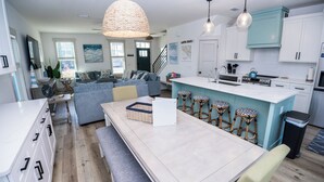 A modern kitchen with white cabinets, a blue island, and a dining area with a bench and stools.