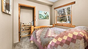 Une chambre à coucher avec un lit en bois, une courtepointe, une fenêtre donnant sur une forêt et une porte menant à un couloir.