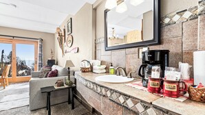 Une salle de bain moderne avec un grand miroir, un lavabo et une machine à café. Il y a une fenêtre donnant sur l’extérieur.