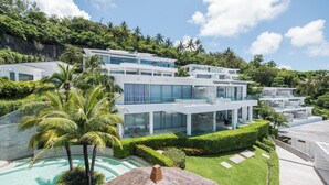 A modern multi-story hotel with a pool, lush greenery, and a thatched roof structure.