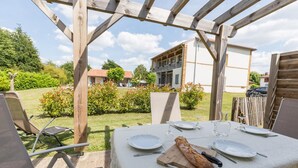 Ulkoilmalounausalue, jossa on neljälle henkilölle katettu pöytä ja jonka ympärillä on puisia pergola-rakenteita.