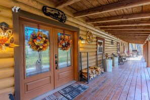 A log cabin with a porch, two glass doors with wreaths, a welcome sign, and a wooden bench.