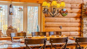 A rustic wooden cabin interior with a dining table, chairs, a chandelier, and a log wall. - Oakland Bear Lair|7BR Luxury Log|Pool, Hot tub (Oakland)