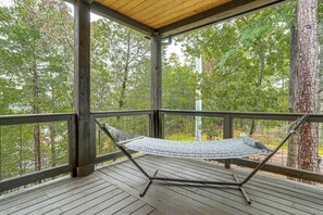 A hammock on a wooden deck with a view of trees.