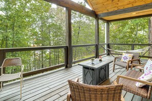 Une terrasse extérieure couverte, aménagée avec des meubles en osier, un barbecue et offrant une vue sur la forêt environnante.